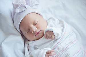 A newborn baby sleeping, wrapped in a blanket.