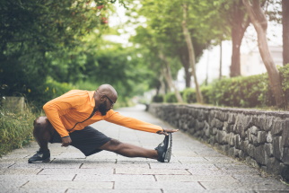 Male in exercise clothes doing a leg stretch outside on a park trail