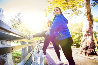 Two people in exercise clothing stretching on a park bench