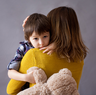 Young child in his mother's arms with a sad look on his face.